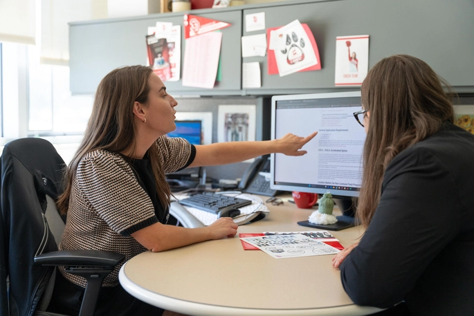 A mentor pointing to a computer screen, working with a student.