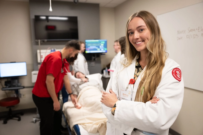 A female medical student stands in front of a simulation exercise.