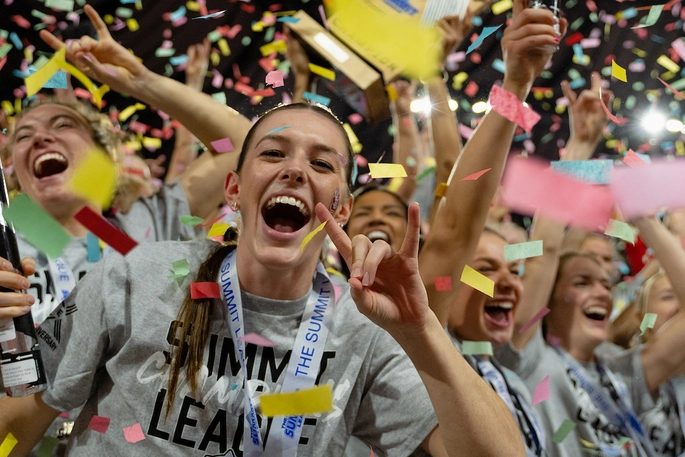 Student athlete wearing champion shirt and medal amidst confetti.
