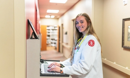 Medical student in a lab coat working on a computer.