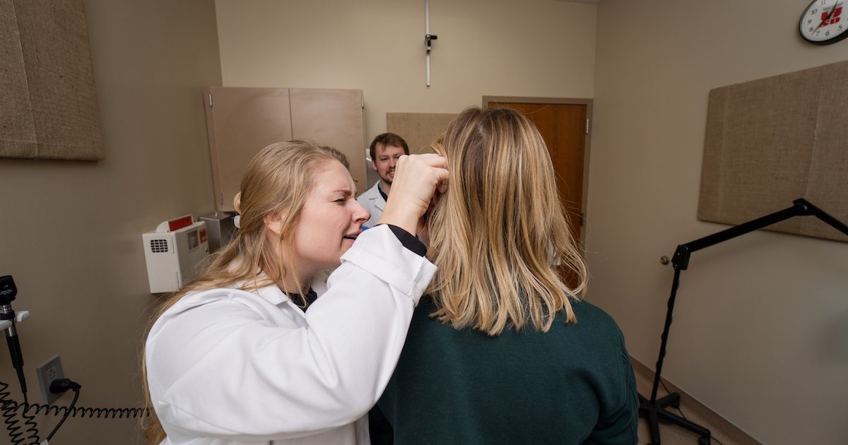 Medical student wearing white coat doing a checkup on a patient in black swestshirt.