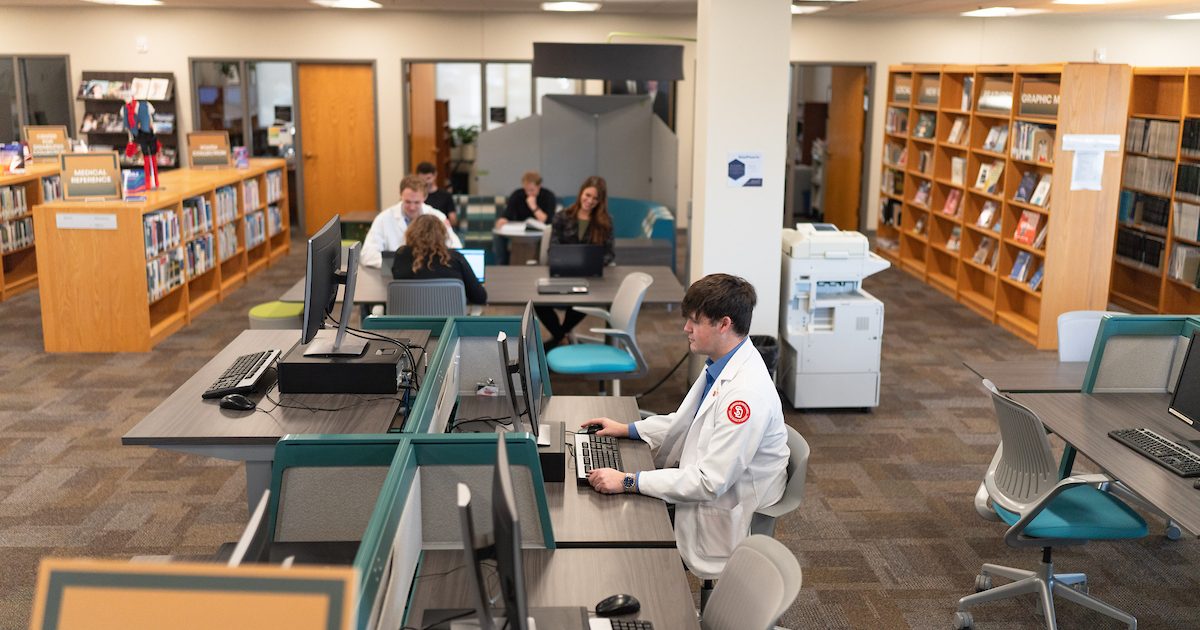 A medical student in white lab coat sitting in the library