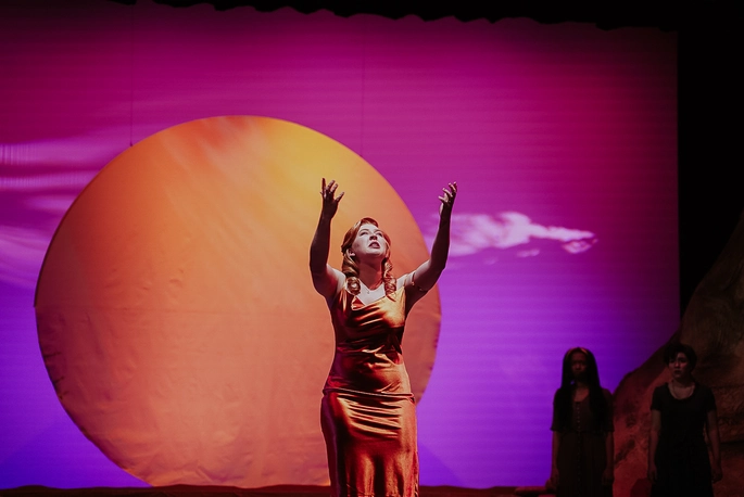A picture of a woman preforming on stage in an orange dress.