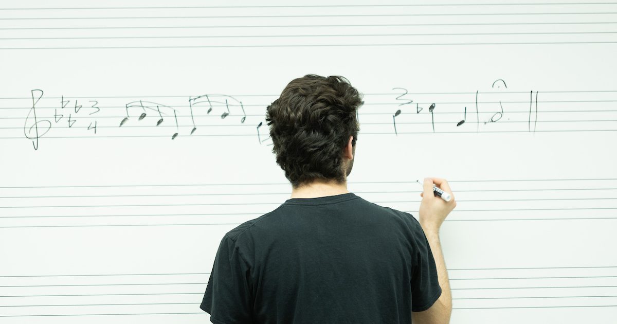A music student drawing notes on a white board in a black t-shirt.