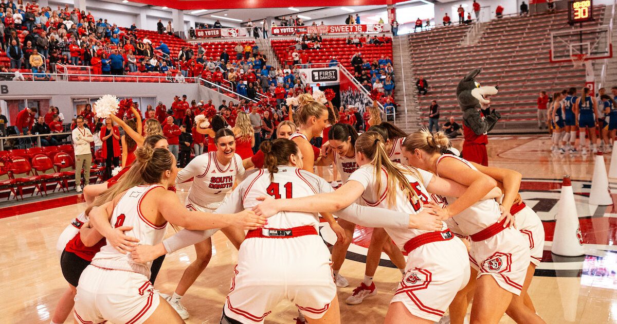 USD Women's basketball team wearing white jerseys in a huddle before a game in the SCSC.
