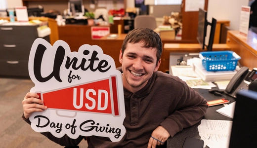 Student posing with Unite for USD Day of Giving sign