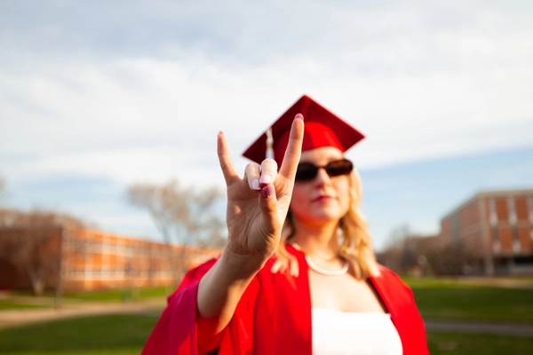 A student in a cap and gown showing the "yotes" symbol.
